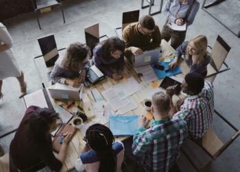 Top view of creative business team sitting at the table at loft office and working. Woman manager brings the document to mixed race group of people. Colleagues discussing the project.