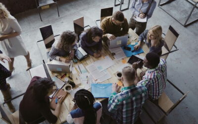 Top view of creative business team sitting at the table at loft office and working. Woman manager brings the document to mixed race group of people. Colleagues discussing the project.